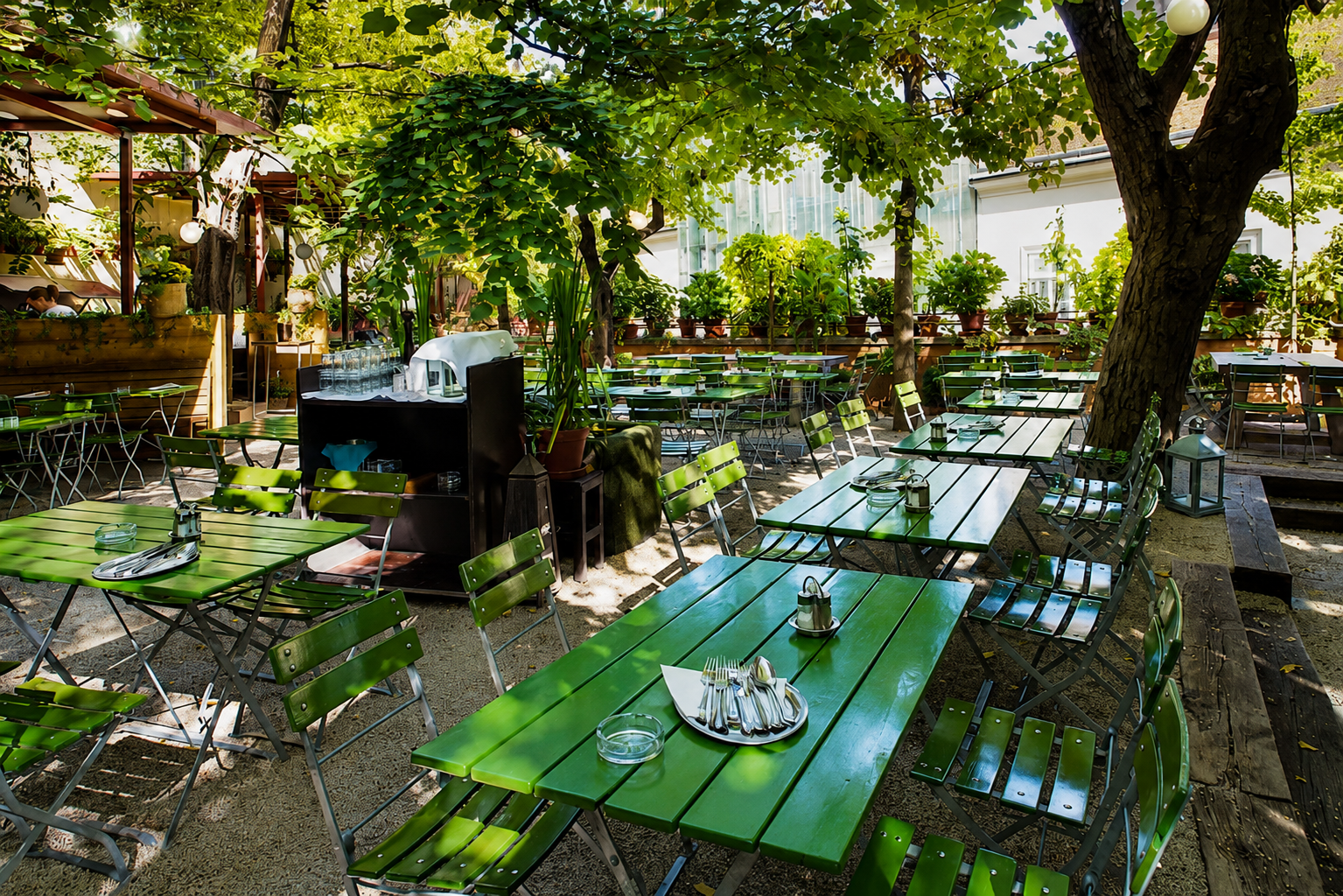 Begrünter Gastgarten des Glacis Beisl im Wiener MuseumsQuartier mit schattigen Sitzplätzen unter alten Bäumen.