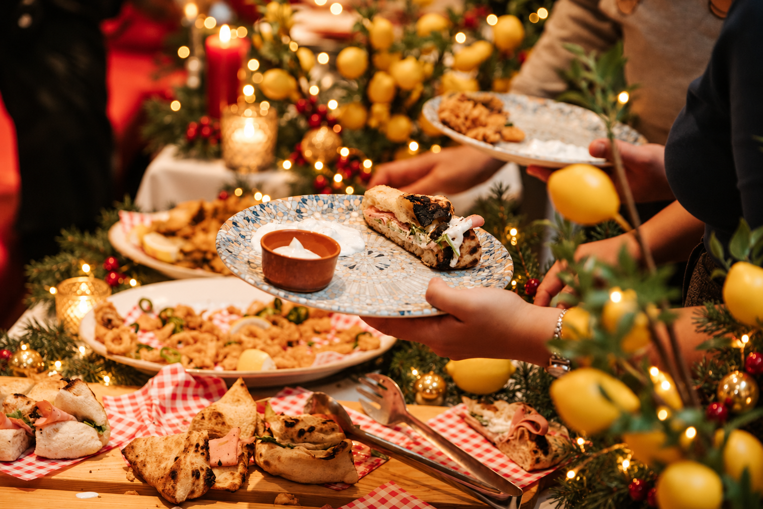 Weihnachtlich gedecktes Buffet mit Fladenbrot, Frittiertem und Zitronen, Gäste halten Teller, Viva La Mamma in Wien